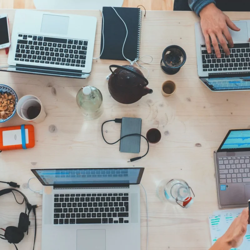 Draufsicht auf einen Tisch, an dem mehrere Personen an Laptops arbeiten