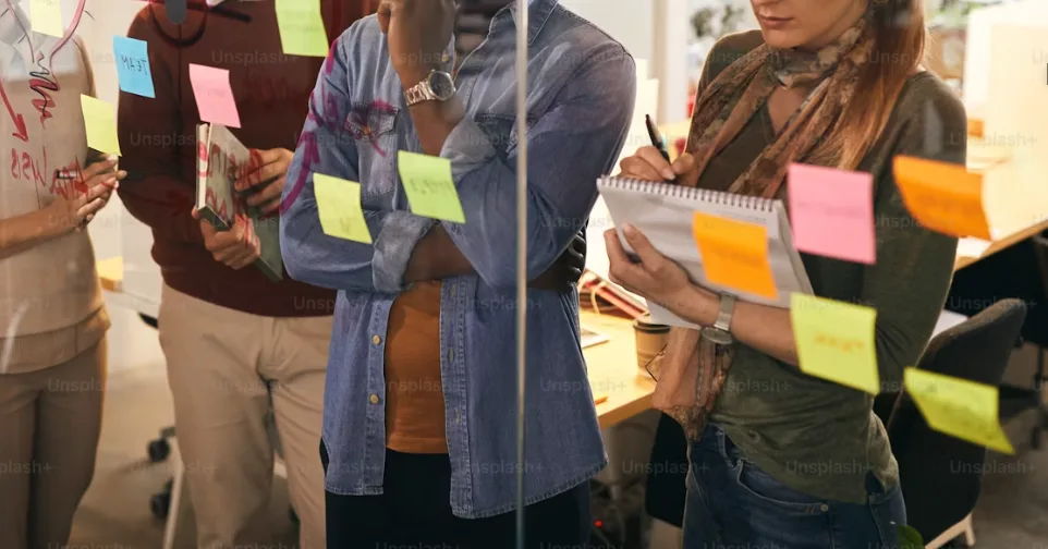 Personen arbeiten in einem Workshop mit Haftnotizen an einer Glaswand